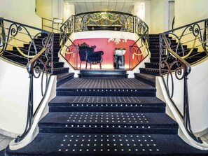 Eine prächtige Treppe mit aufwendigen schwarzen Geländern, eine rote Wand mit einer Blumenkomposition und ein schwarz bezogener Sessel.
