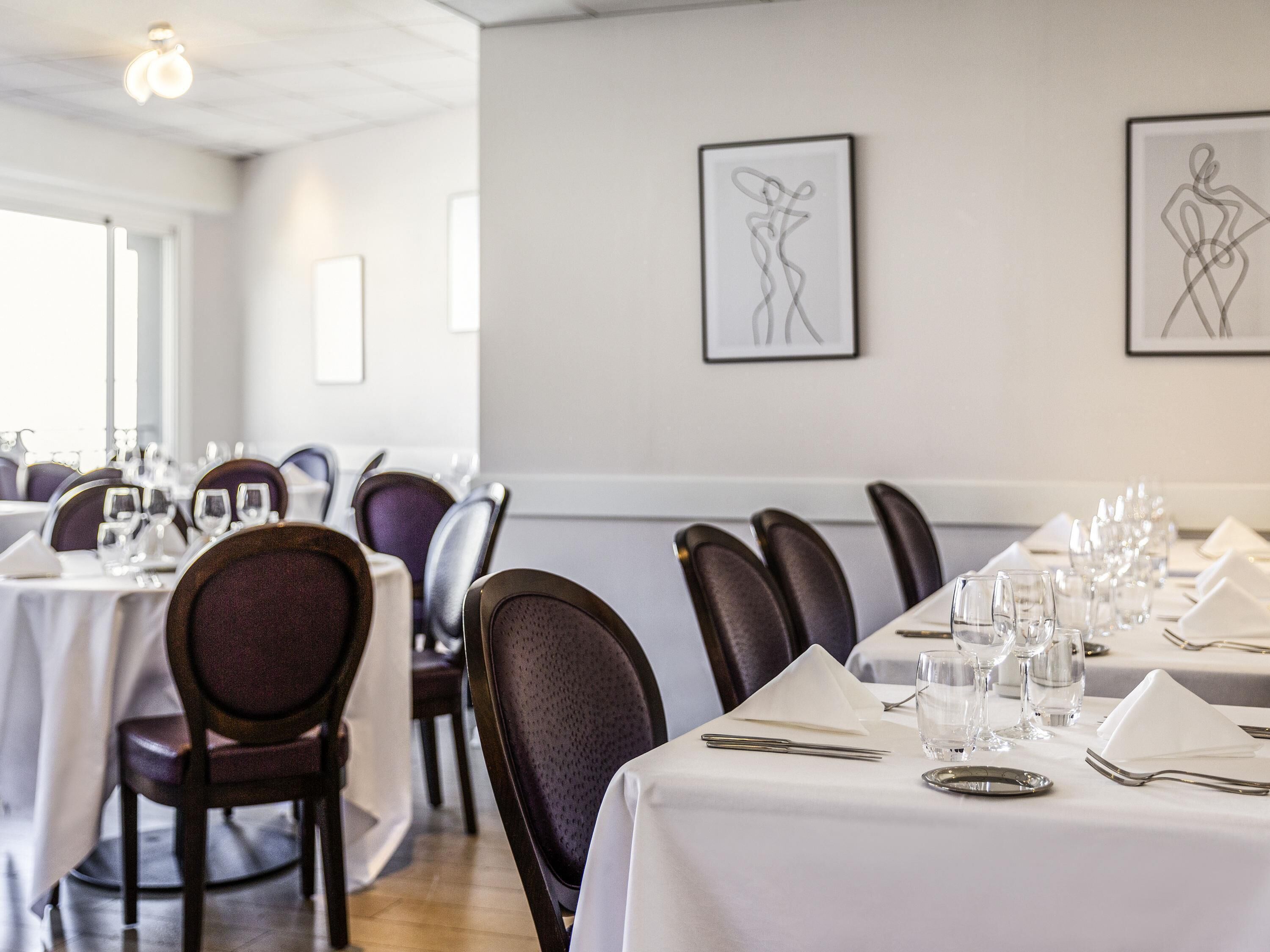 A dining area with tables set for service, chairs, and framed artwork on the wall.