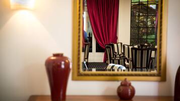 A mirror reflecting a room with a red curtain, striped chairs, and a vase on a wooden table.