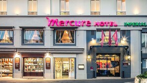 Un hotel con un llamativo letrero de 'Mercure Hotel', una fachada con escaparates de vidrio y una bandera en el exterior.
