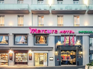 Un hotel con un llamativo letrero de 'Mercure Hotel', una fachada con escaparates de vidrio y una bandera en el exterior.