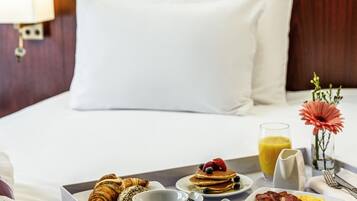 Un plateau de petit-déjeuner joliment préparé, avec des croissants, des crêpes, des fraises, des myrtilles et du bacon, posé sur un lit recouvert de draps blancs et doté d’une tête de lit en bois.