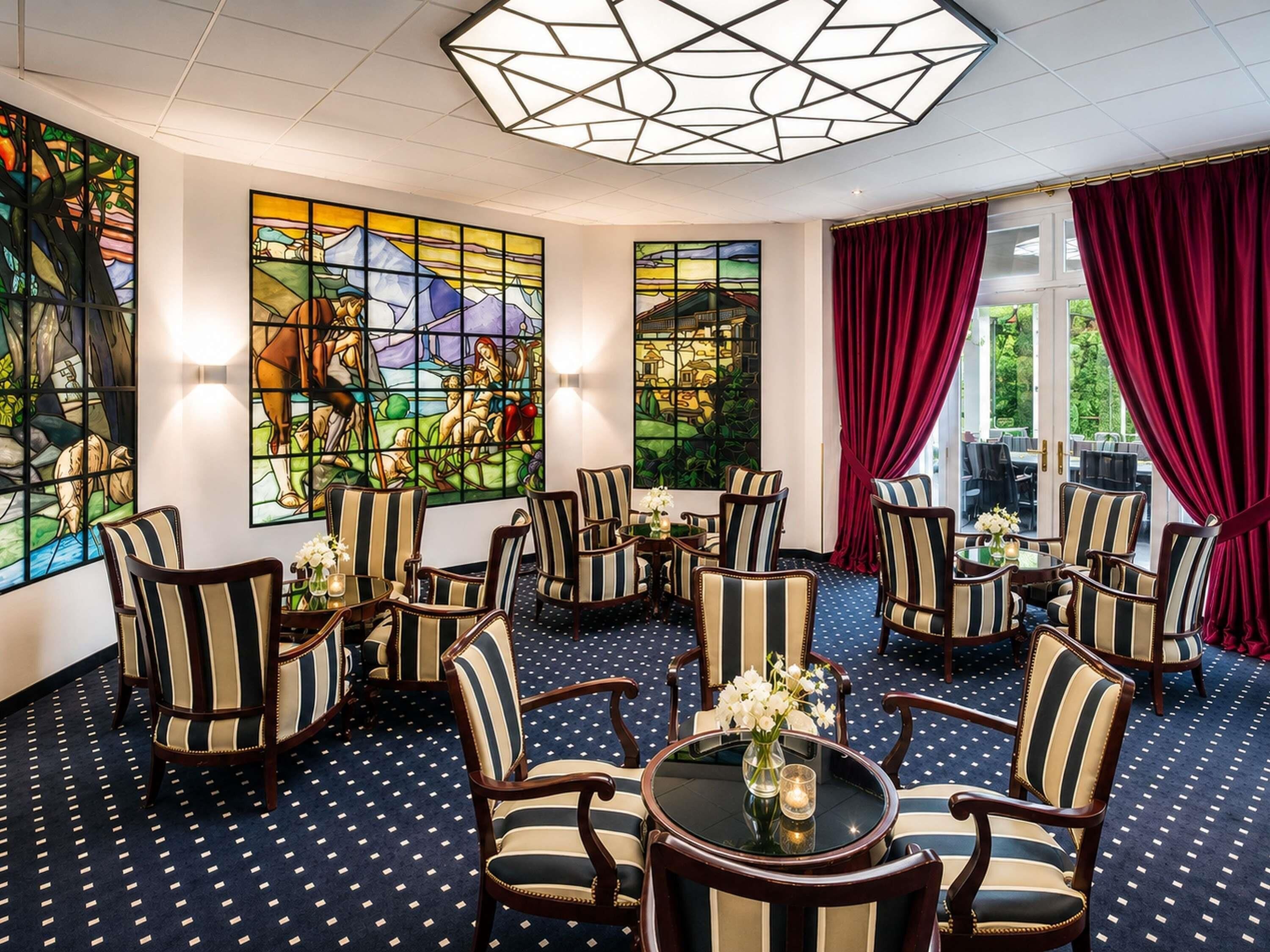 A room with striped chairs, a round table, and large windows with stained glass.