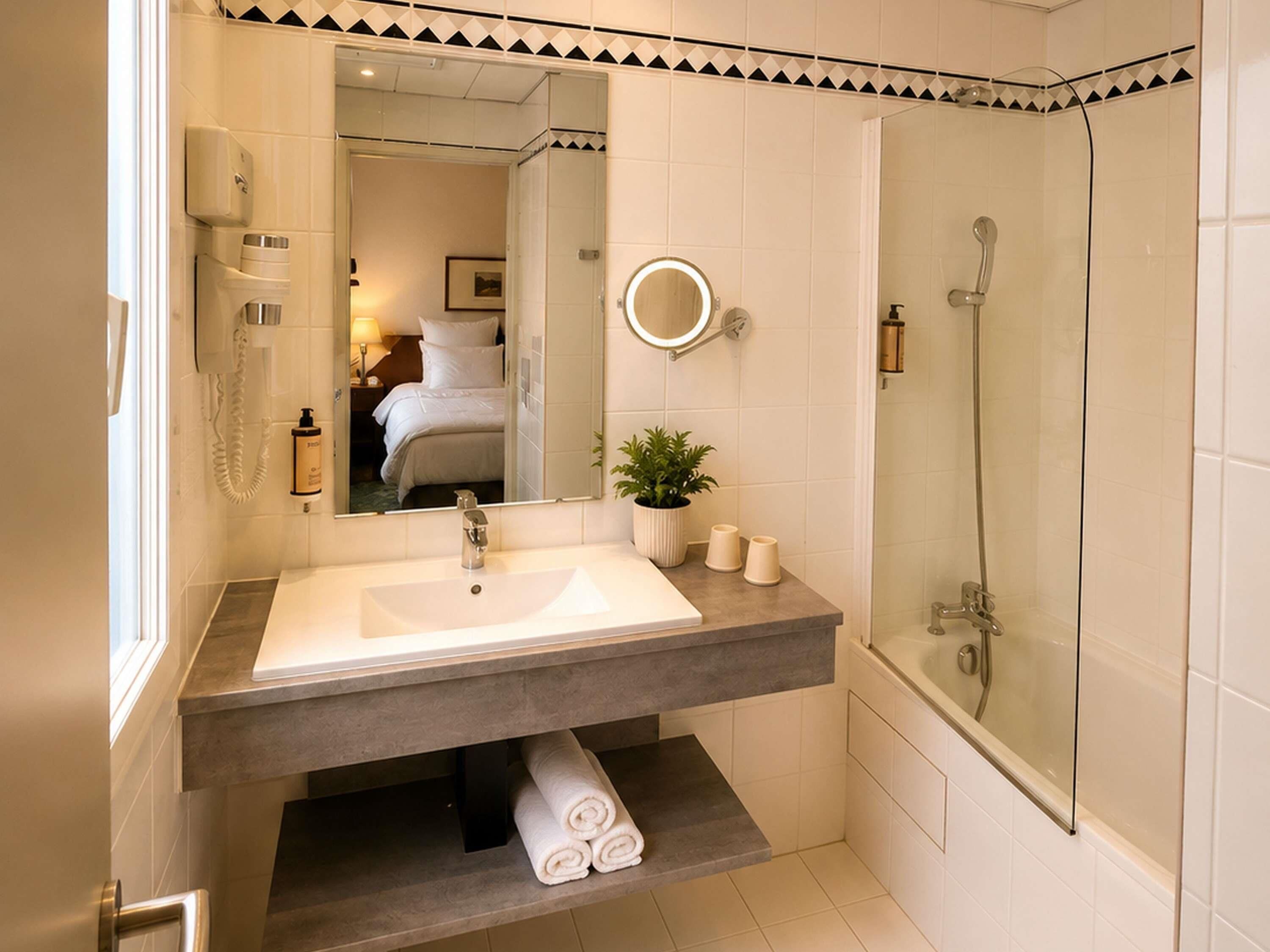 A bathroom with a large mirror, a sink, a shower, and a toilet.