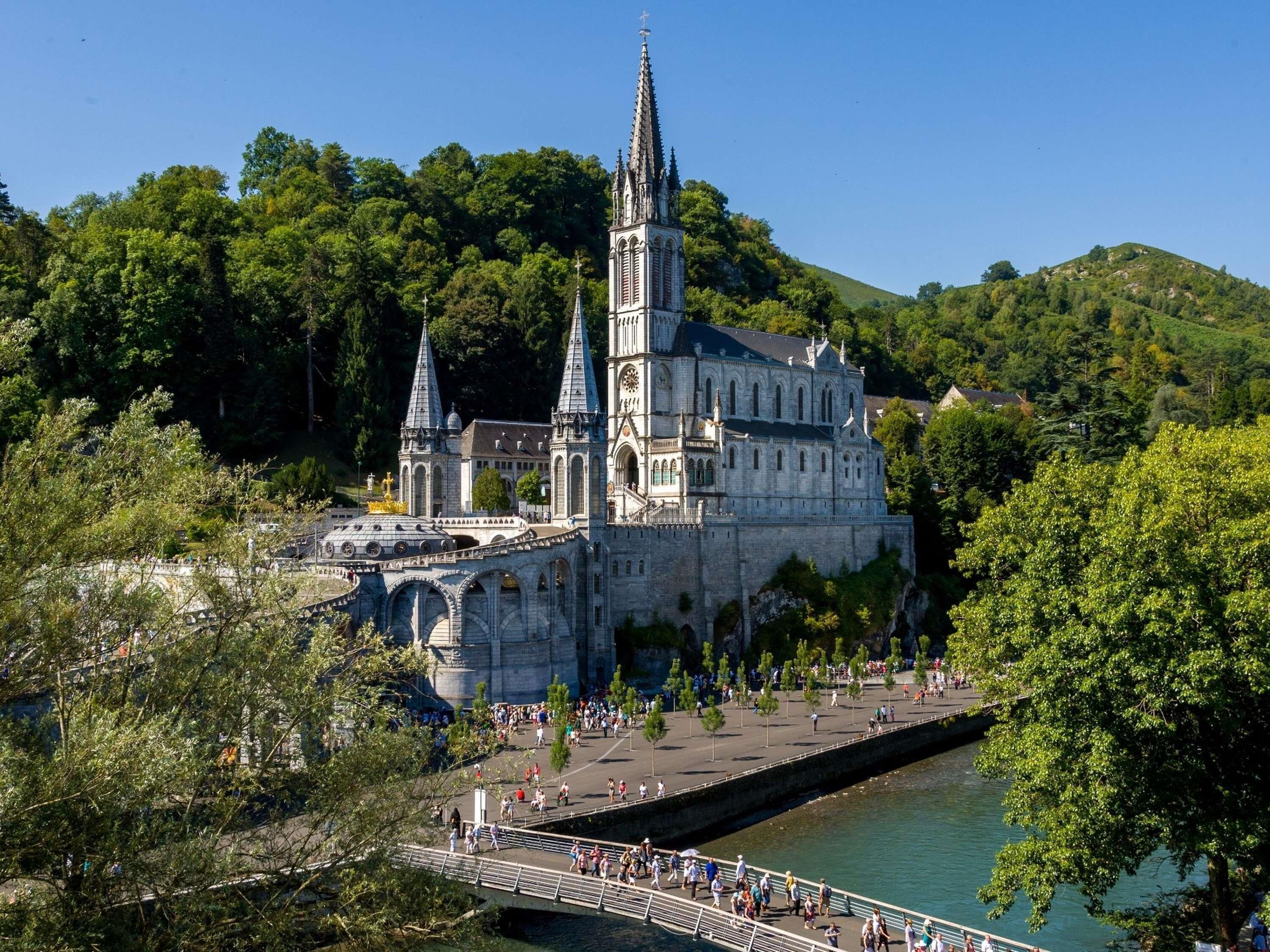 A historic castle with a prominent tower, situated by a river with a pedestrian bridge.