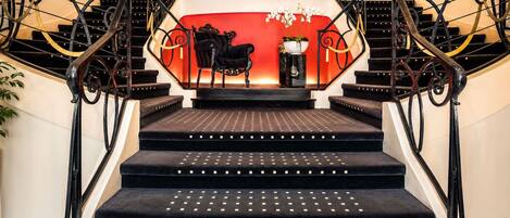 A grand staircase with ornate black railings and a red wall at the top.