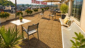 Una terraza en la azotea con mobiliario exterior, plantas en macetas y sombrillas.