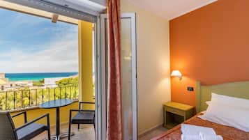 Ein Hotelzimmer mit Balkon, einem Bett mit weißer Bettwäsche, einem kleinen Nachttisch und Meerblick.
