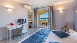 Habitación de hotel con una cama, un escritorio, una silla y un televisor. Cuenta con un balcón con vistas al mar.