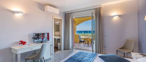 A hotel room with a bed, a desk, a chair, and a TV. There is a balcony with a view of the sea.