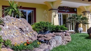 Exterior de un hotel con jardín de rocas, fuente de agua y un letrero que dice 'Hotel Rosa del Viento'.