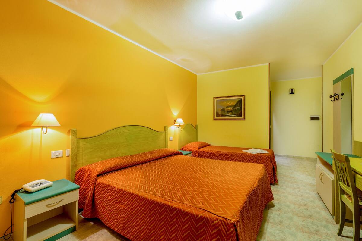 A hotel room with two beds, a desk, a chair, a lamp, and a painting on the wall.