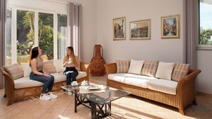 Una sala de estar con muebles de mimbre, una mesa de centro de vidrio y obras de arte en la pared.
