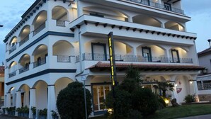 Un hotel de varios pisos con balcones, un llamativo letrero que dice 'HOTEL' y un jardín bien cuidado.