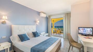 Habitación de hotel con una cama grande, un escritorio con televisor y un balcón con barandilla amarilla.