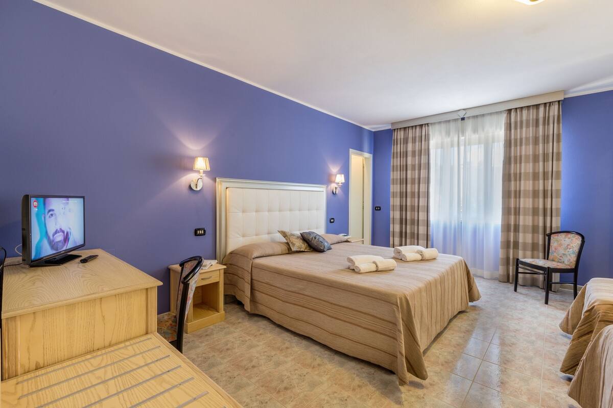 A hotel room with a large bed, a desk, a chair, and a television.