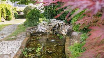 A small pond with a stone border, surrounded by lush greenery and a stone pathway.