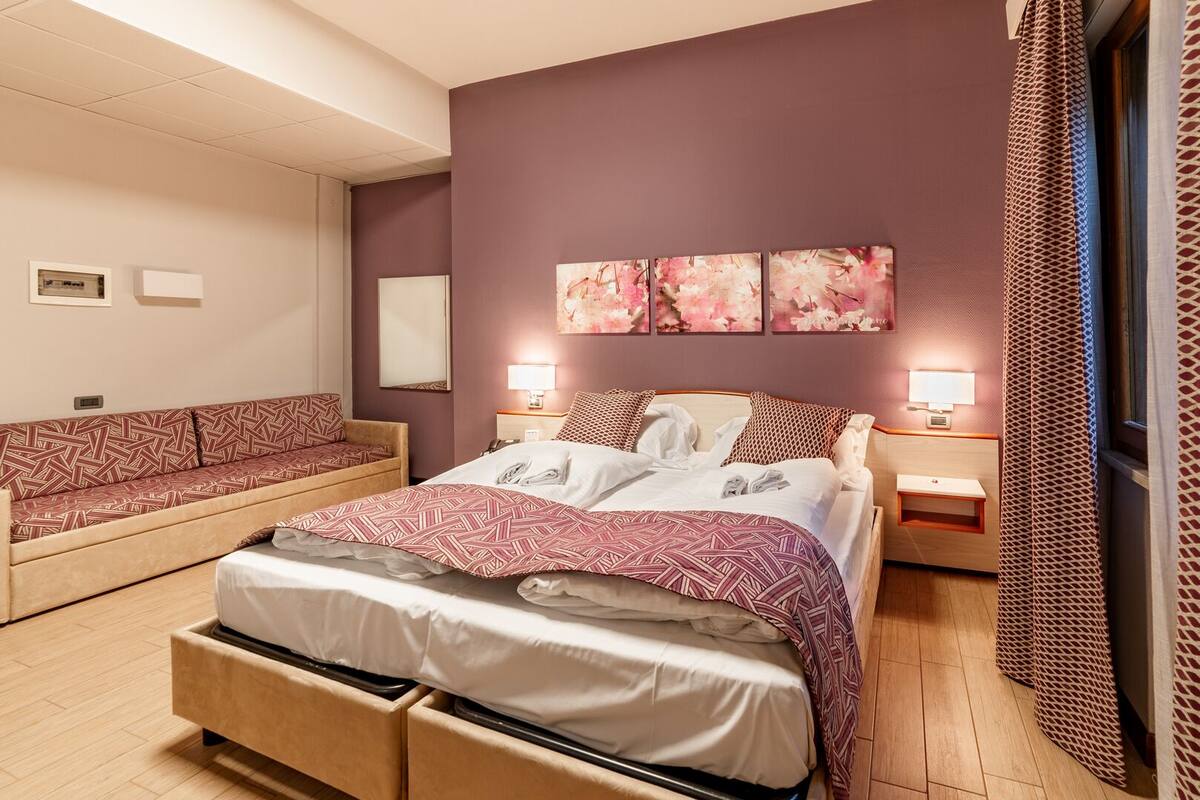 Un dormitorio con cama, sofá y mesita de noche con lámpara.