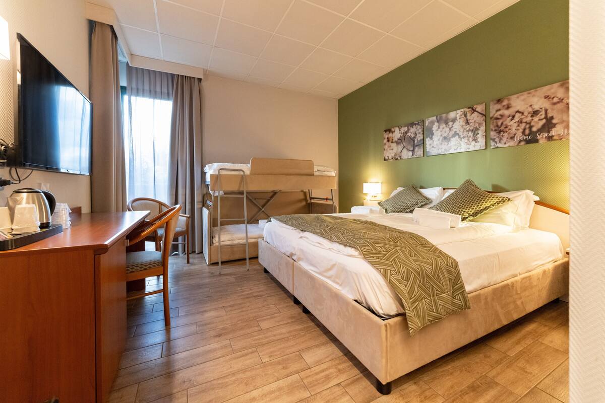 Habitación de hotel con cama, escritorio, silla, televisión y obras de arte en la pared.