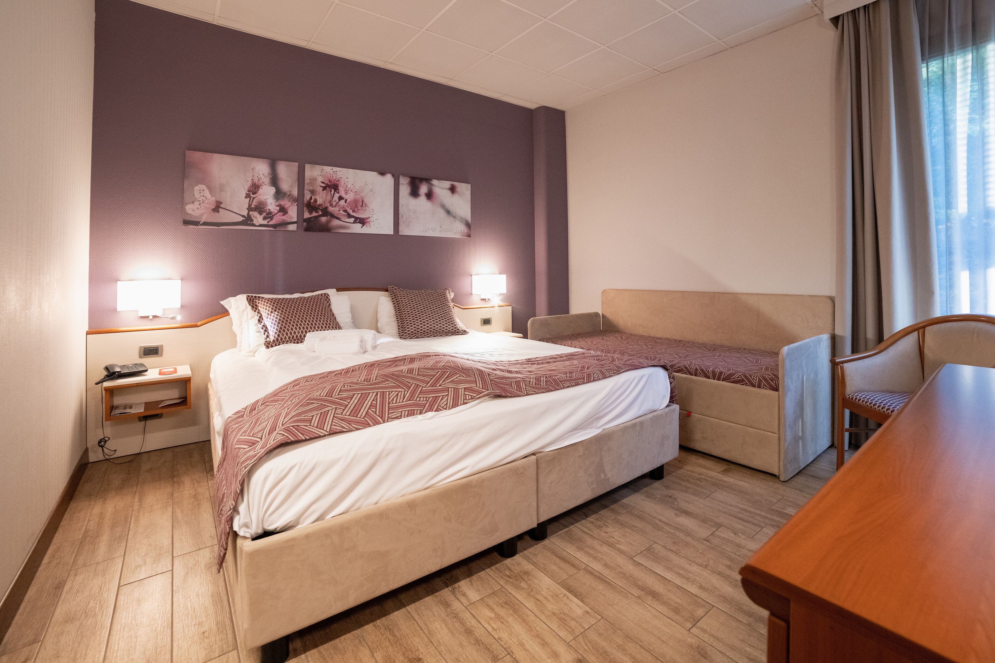 Una habitación de hotel con una cama, una silla, un escritorio y obras de arte en la pared.