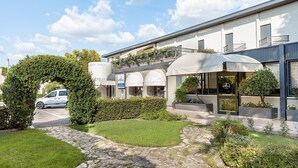 A hotel with a stone pathway leading to a covered outdoor seating area, surrounded by greenery and a clear sky. - Hotel All'Orso (Roncade)