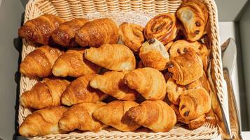 Una cesta de mimbre llena de diversos pasteles, incluyendo croissants y un pastel con remolino de chocolate.