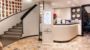A hotel lobby with a reception desk, a staircase, and a wall decorated with various badges. - Hotel All'Orso (Roncade)