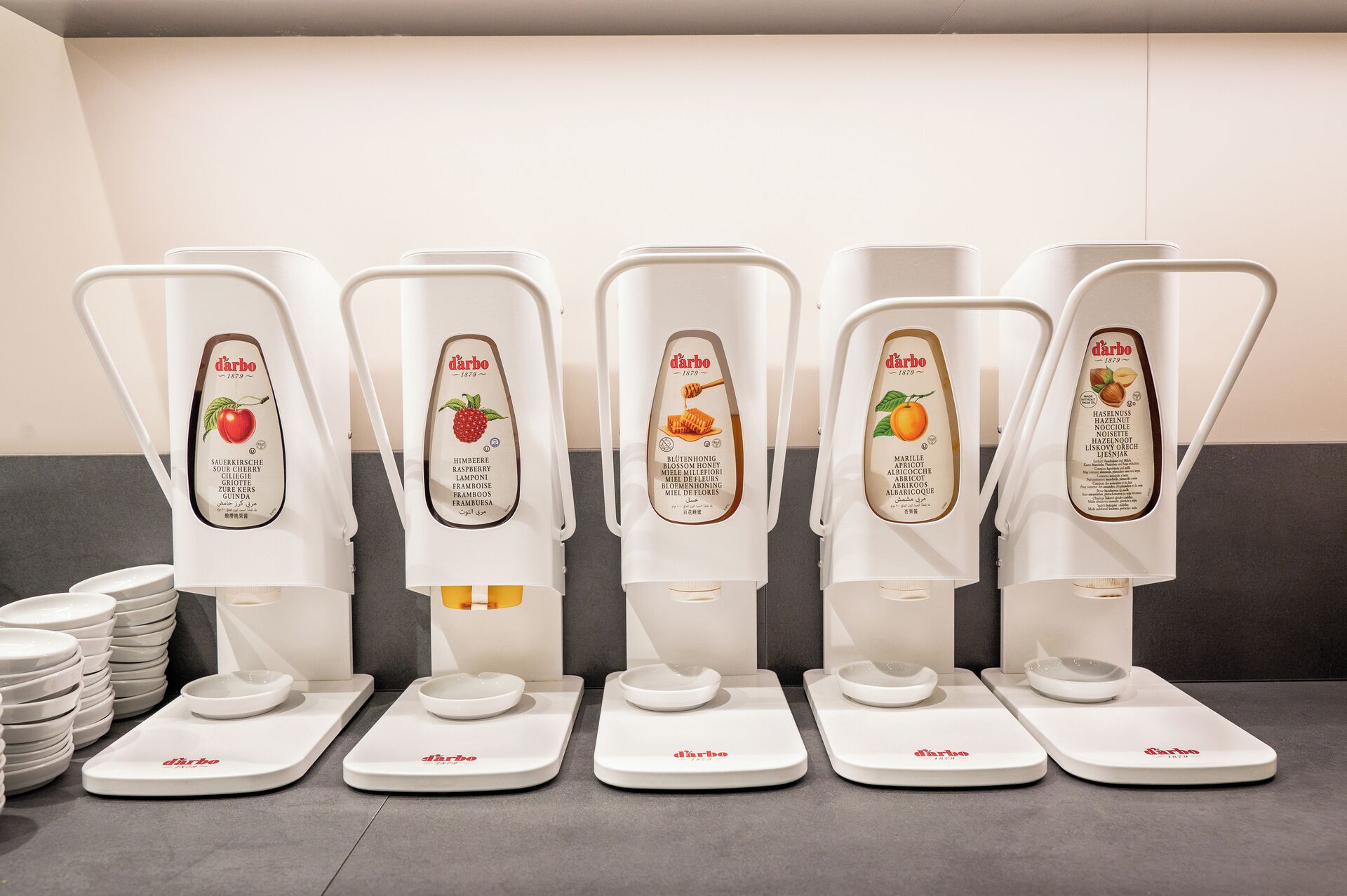 A row of white dispensers with labels indicating different flavors, each with a bowl on a base.