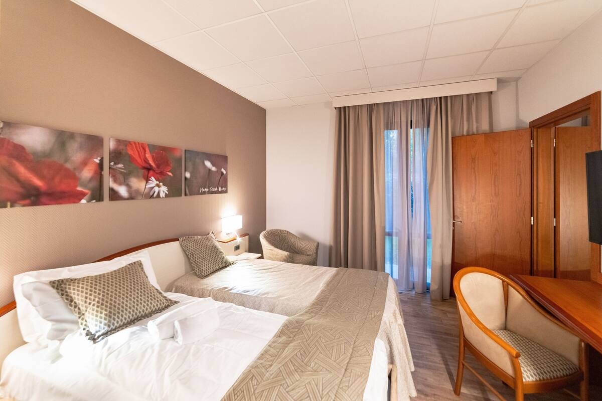 Habitación de hotel con dos camas, un escritorio, una silla, un televisor y una ventana con cortinas.