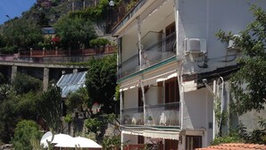 A two-story building with a balcony, potted plants, and a tiled roof. - Hotel Villa Greta (Taormina)