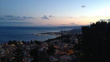 A coastal cityscape at dusk with a view of the sea and a distant pier.