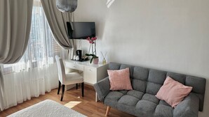 A modern living room with a grey sofa, a white desk, and a large window with sheer curtains. - Hotel Villa Greta (Taormina)