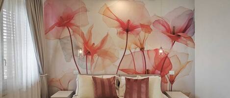 A modern bedroom with a large bed, a wall mural of flowers, and a bedside table with a lamp.
