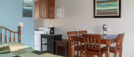 A room with a bed, a desk, a chair, and a dining table.