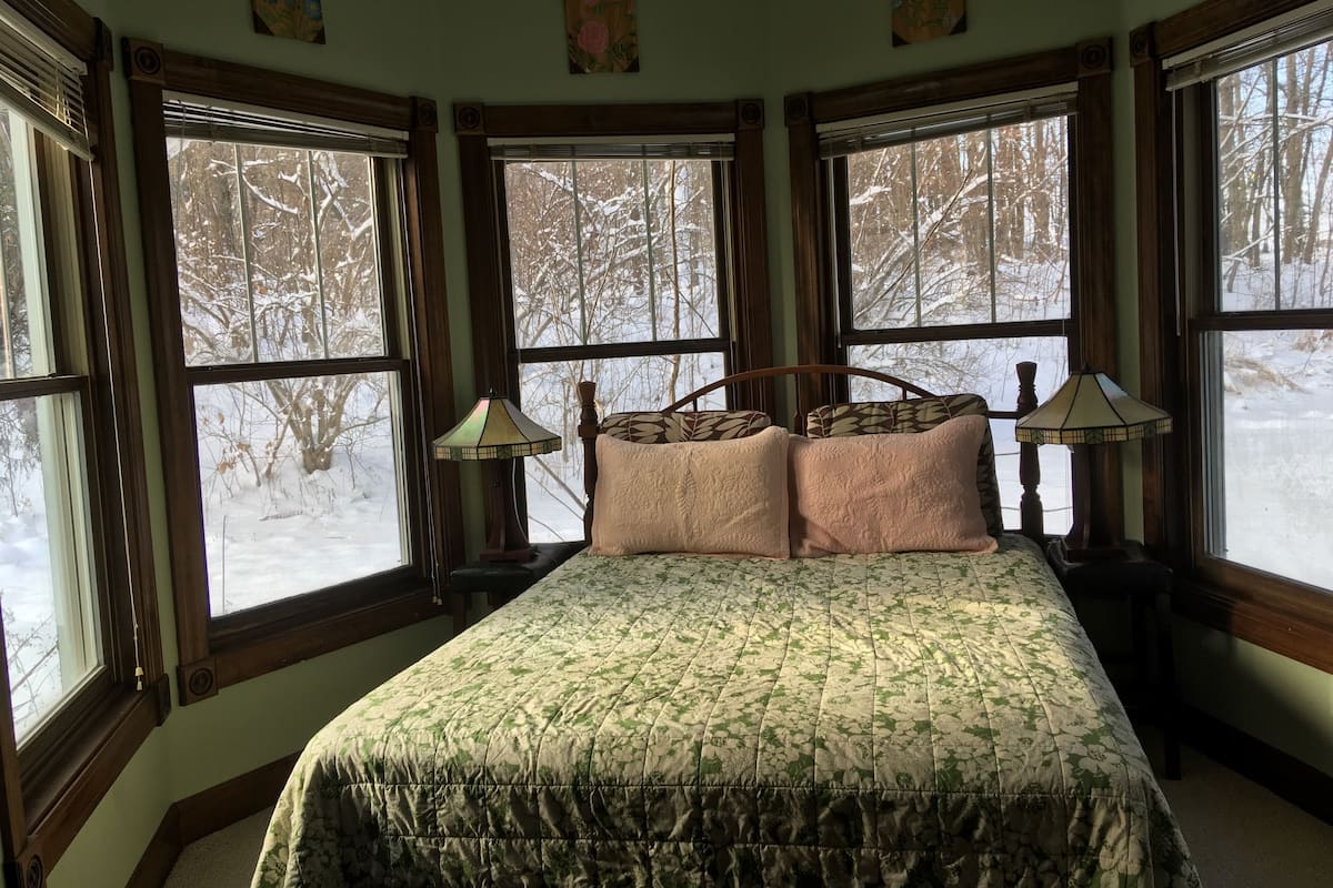 Un dormitorio con una cama grande, dos lámparas de noche y varias ventanas que ofrecen vistas a un paisaje nevado.
