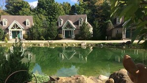 A serene lakeside view with two houses and a clear reflection in the water. - Spruce Hill Inn and Cottages (Mansfield)