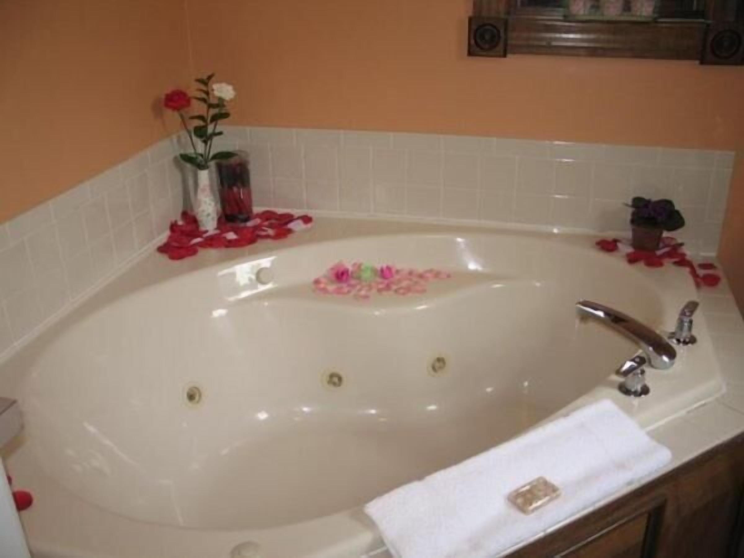 A bathtub with rose petals and a small vase of flowers.
