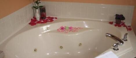 A bathtub with rose petals and a small vase of flowers.