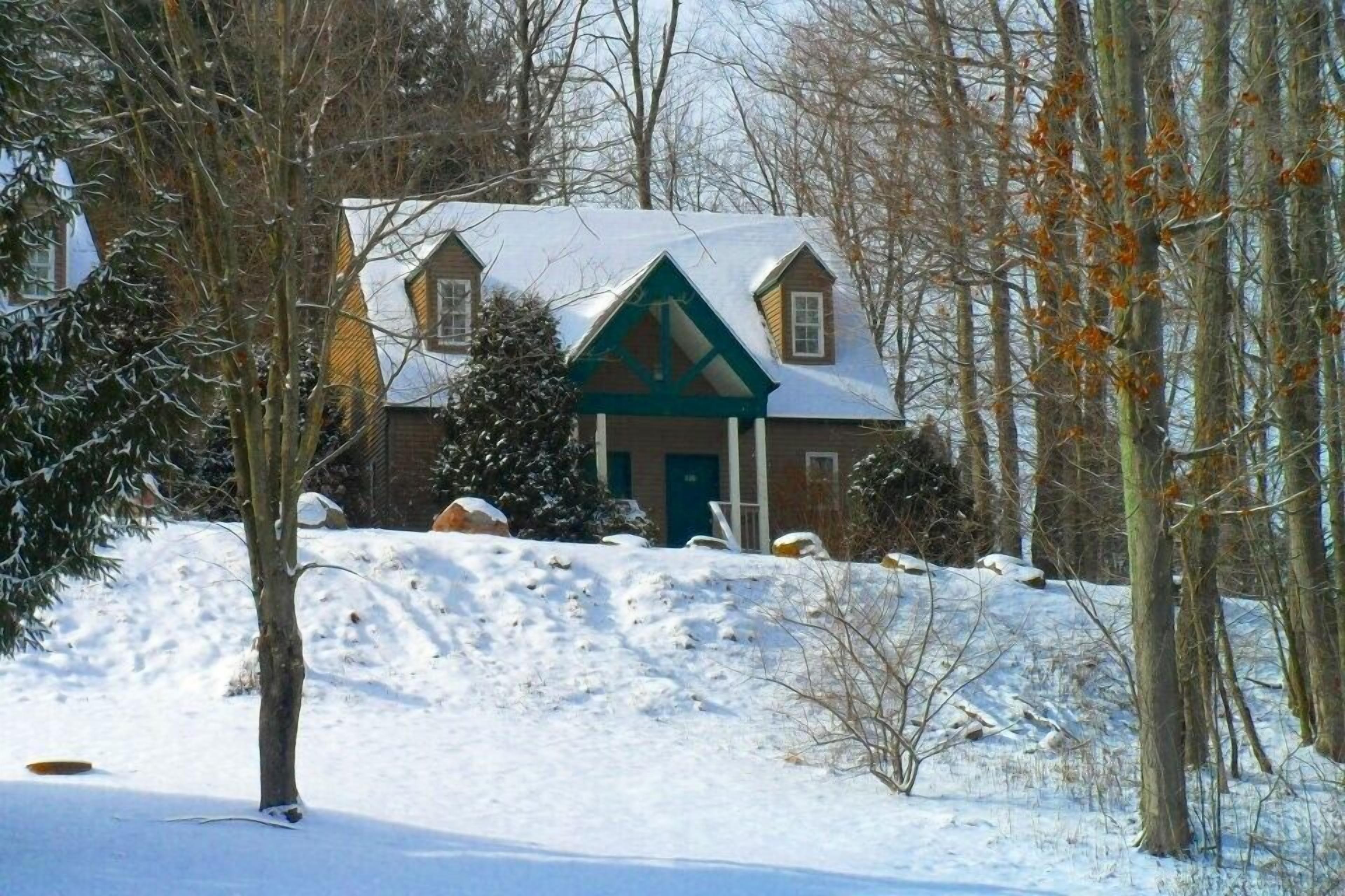 A house with a steeply pitched roof, a front porch, and a snow-covered landscape.