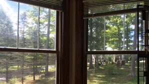 A room with large windows offering a view of a forested area with a playground. - Spruce Hill Inn and Cottages (Mansfield)