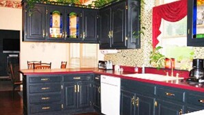 A kitchen with dark cabinetry, a red countertop, and a window with a red curtain. - Spruce Hill Inn and Cottages (Mansfield)