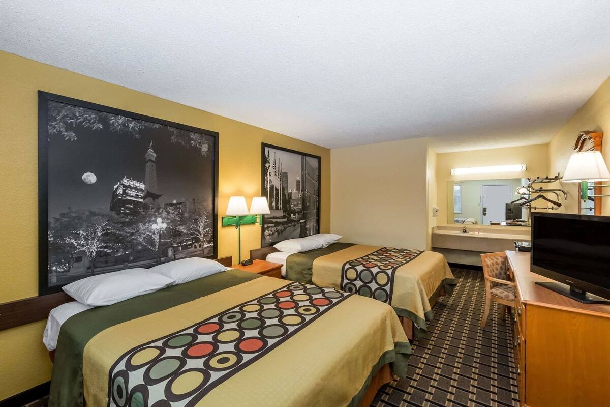 A hotel room with two beds, a TV, a desk, and a bathroom mirror.