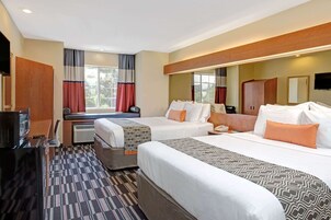 Habitación de hotel con dos camas, televisor, escritorio y un ventanal grande con cortinas.