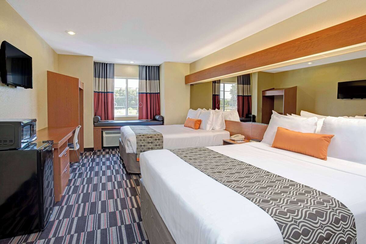 A hotel room with two beds, a desk, a TV, and a window with curtains.