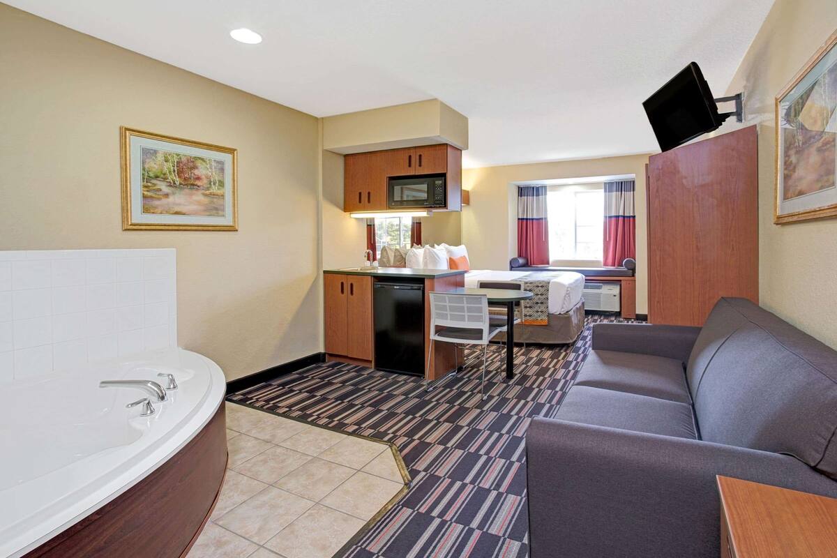 A compact hotel room with a bathroom, kitchenette, and a sofa.