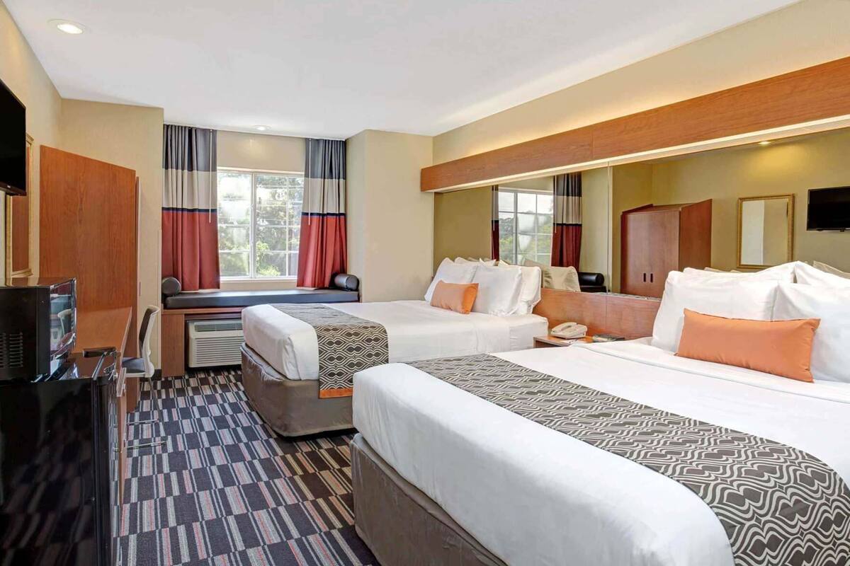 A hotel room with two beds, a TV, a desk, and a window with curtains.
