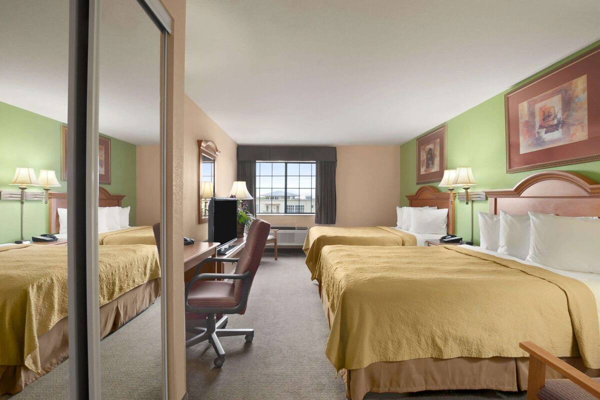 Ein Hotelzimmer mit zwei Betten, einem Schreibtisch, einem Sessel, einem Fernseher und einem Fenster.