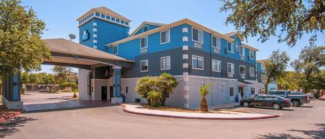 Un hotel de varios pisos con fachada azul y gris, un acceso cubierto y palmeras en la entrada.