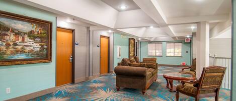 A hotel lobby with a patterned carpet, a sofa, a chair, and a painting on the wall.