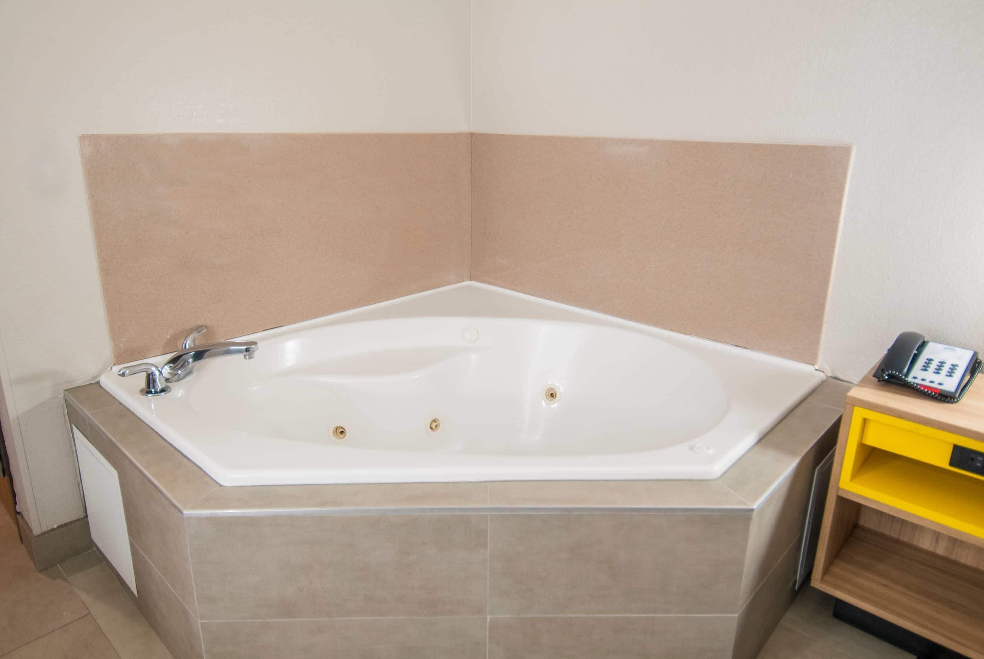 Un baño con una bañera grande, una mesita de madera pequeña con un teléfono, y un estante amarillo.